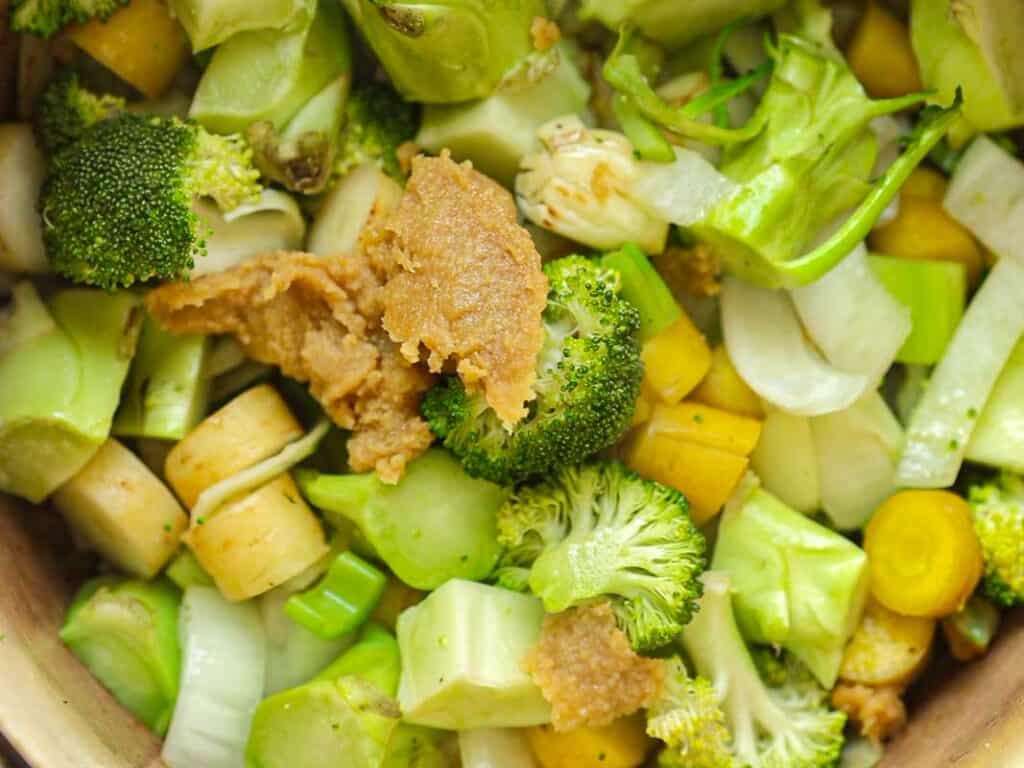 Close-up of a stir-fry dish featuring broccoli florets, and miso paste. The vegetables are vibrant and the sauce appears thick, coating the ingredients partially.